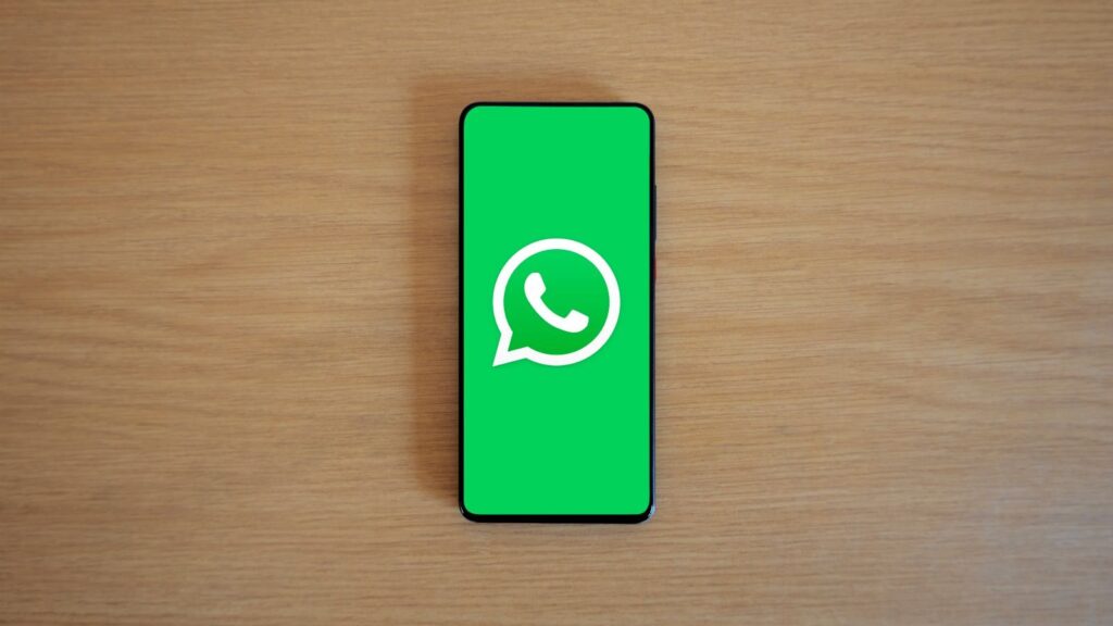 Top view of smartphone displaying WhatsApp logo on a wooden background, representing technology and communication.