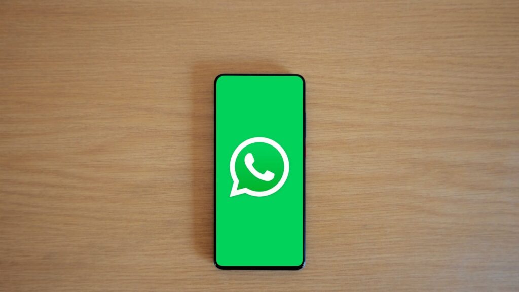 Top view of smartphone displaying WhatsApp logo on a wooden background, representing technology and communication.