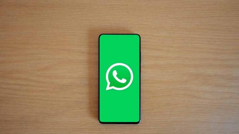 Top view of smartphone displaying WhatsApp logo on a wooden background, representing technology and communication.