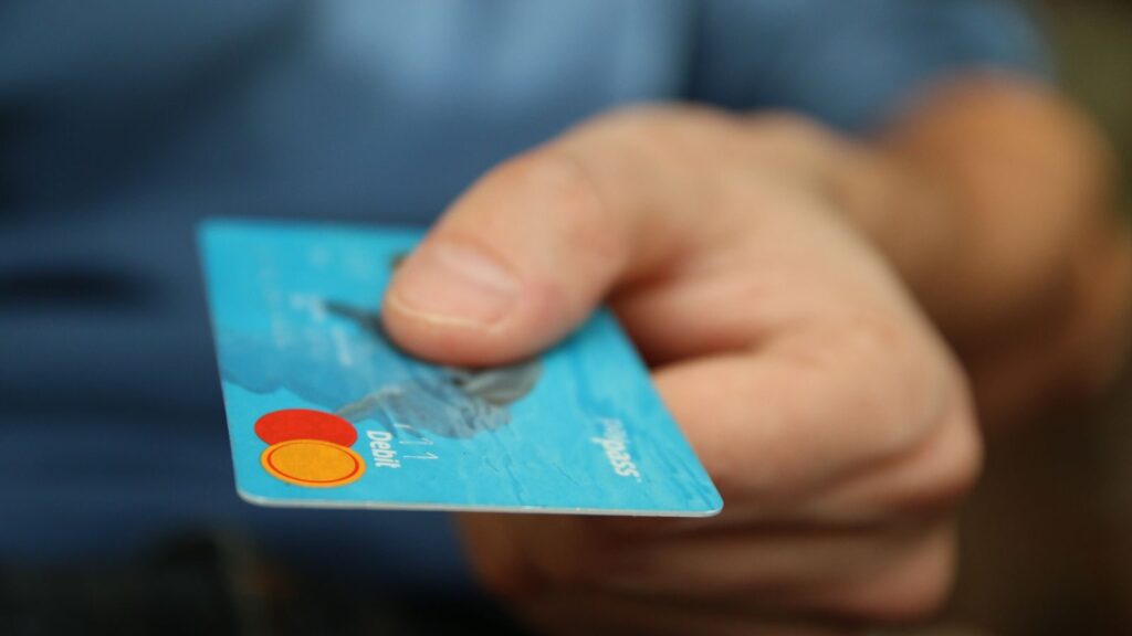 A close-up shot of a hand offering a blue debit card for payment.