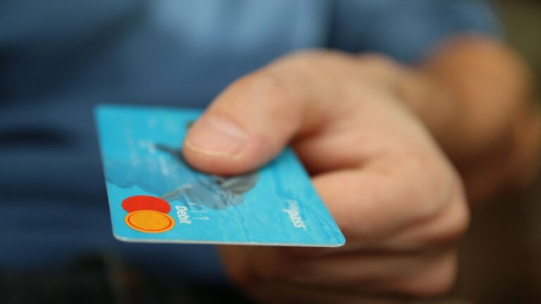 A close-up shot of a hand offering a blue debit card for payment.