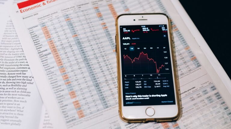 Smartphone displaying stock market data on papers with financial charts.