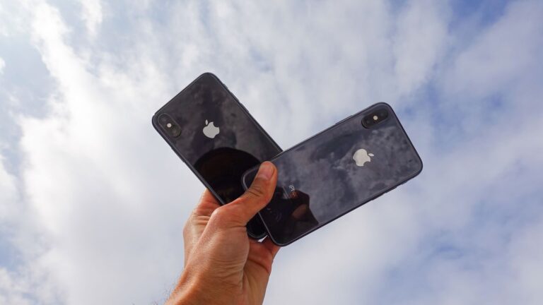 Close-up of a hand holding two smartphones against a cloudy sky, showcasing modern technology.