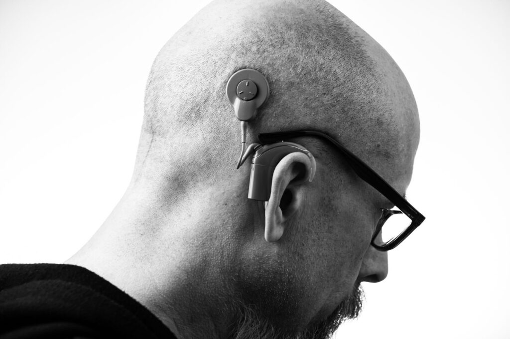 Black and white profile of a man wearing glasses and a hearing aid, studio shot.