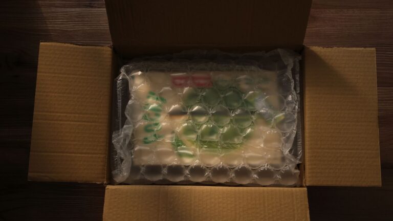 Open cardboard box displaying bubble-wrapped content, photographed indoors with soft lighting.