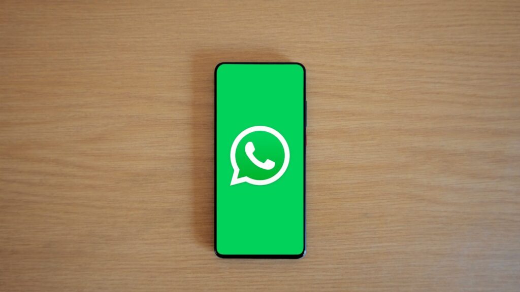 Top view of smartphone displaying WhatsApp logo on a wooden background, representing technology and communication.