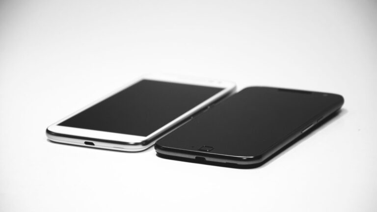 Two smartphones, one black and one white, placed on a white surface, showcasing modern design.