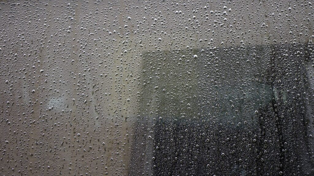 Close-up of a rain-drenched window covered in water droplets, showcasing abstract urban atmosphere.