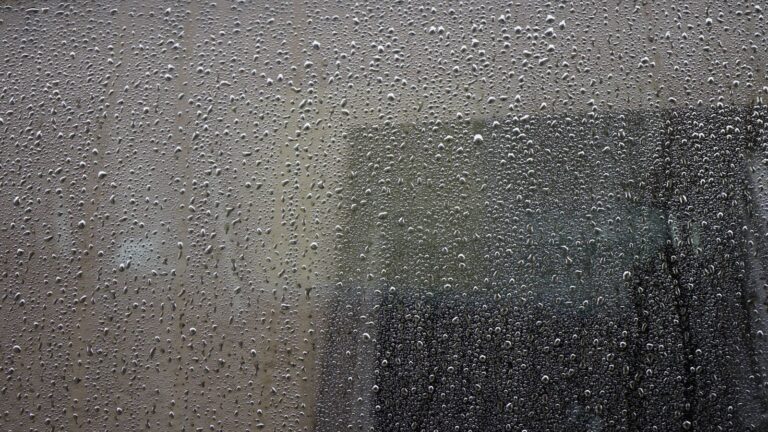 Close-up of a rain-drenched window covered in water droplets, showcasing abstract urban atmosphere.