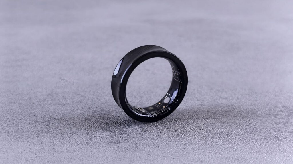 A modern black smart ring with visible circuitry resting on a textured concrete surface.