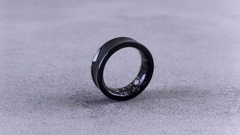 A modern black smart ring with visible circuitry resting on a textured concrete surface.