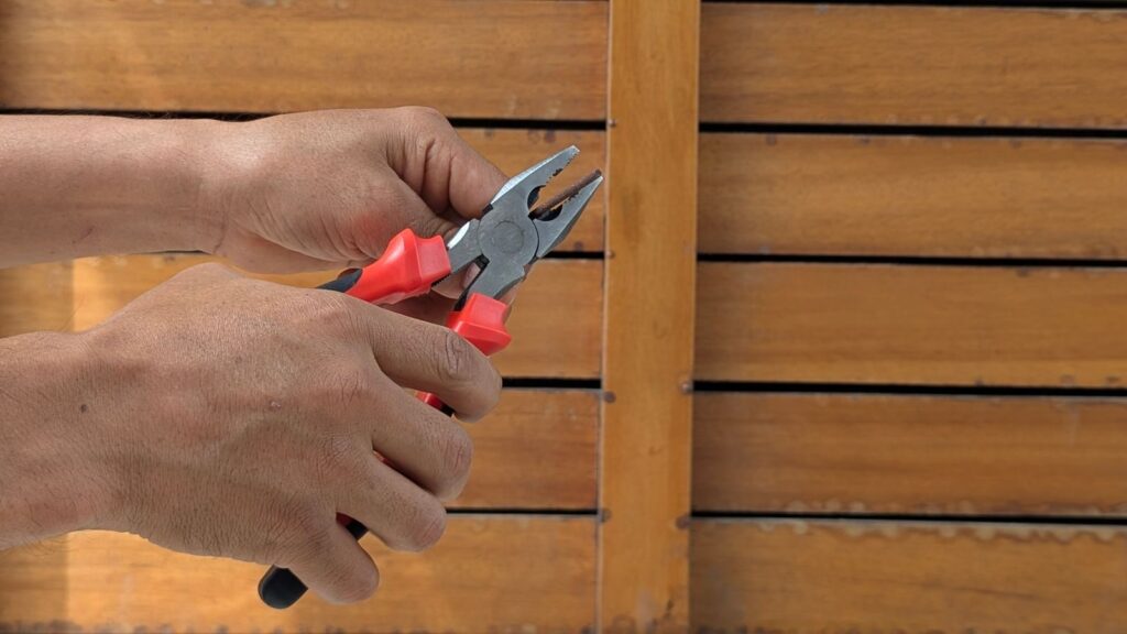 A detailed view of hands holding red pliers against a wooden backdrop, depicting a DIY or repair scene.