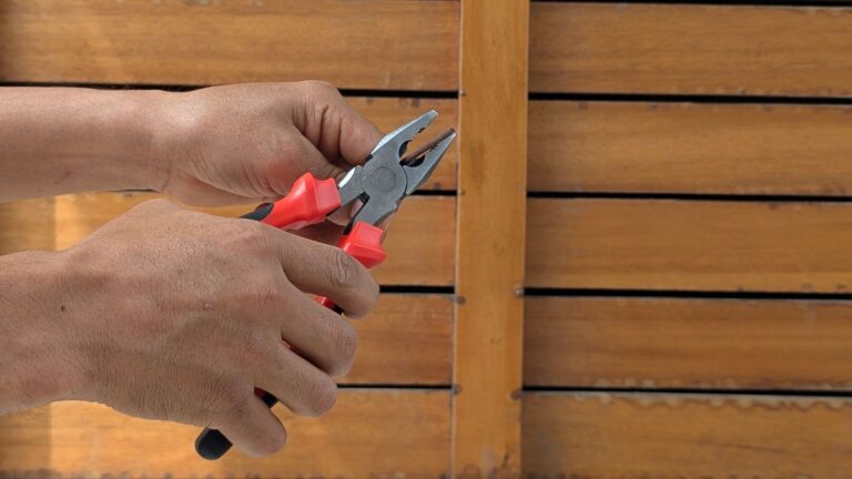 A detailed view of hands holding red pliers against a wooden backdrop, depicting a DIY or repair scene.