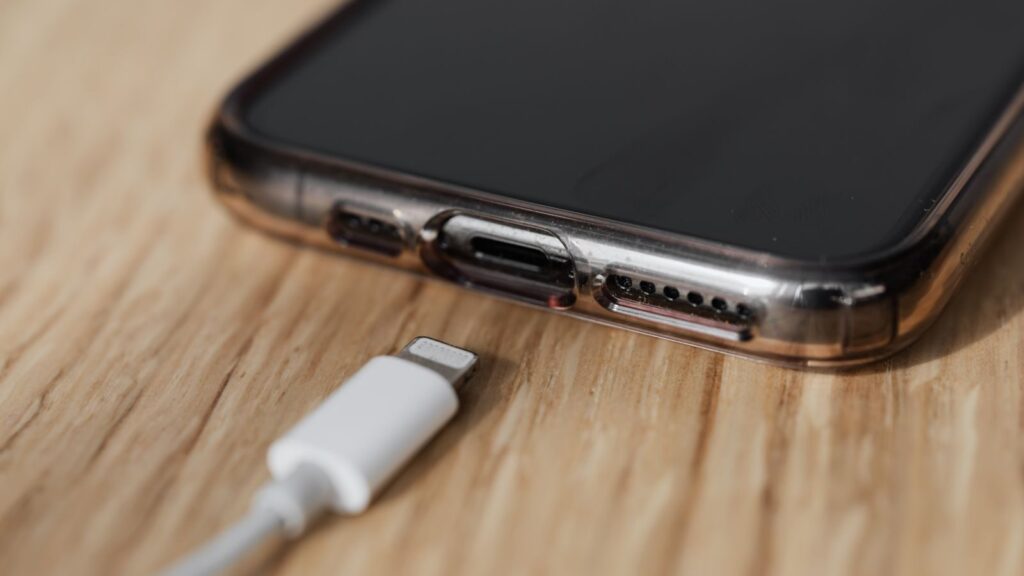 Modern cellphone in transparent cover with closeup of charging input and mobile phone white charger cable usb connector on wooden table