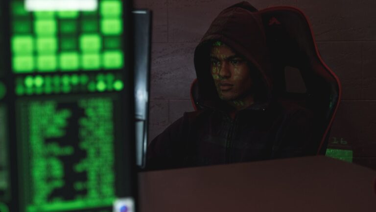 Hooded programmer intensely focused on computer screen, ensuring data protection and cyber security.