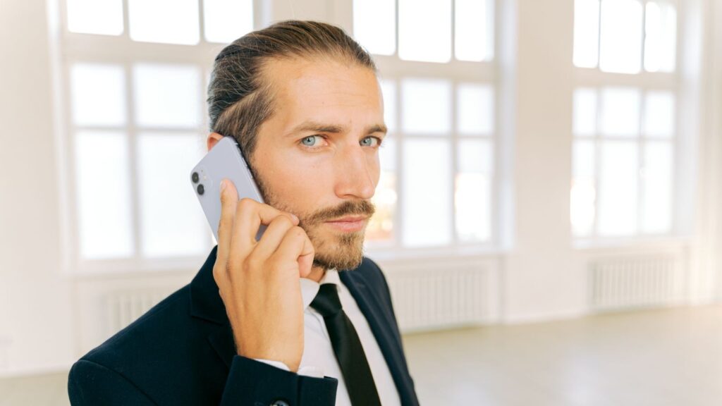 Professional man in a suit holding a smartphone in a bright indoor setting.