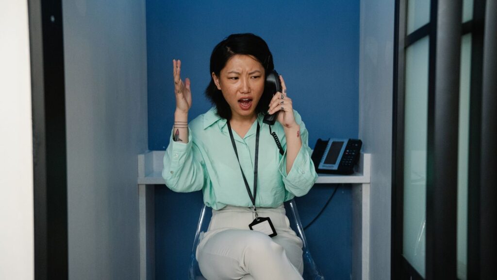 An east Asian woman expressing frustration during a phone call at the workplace.