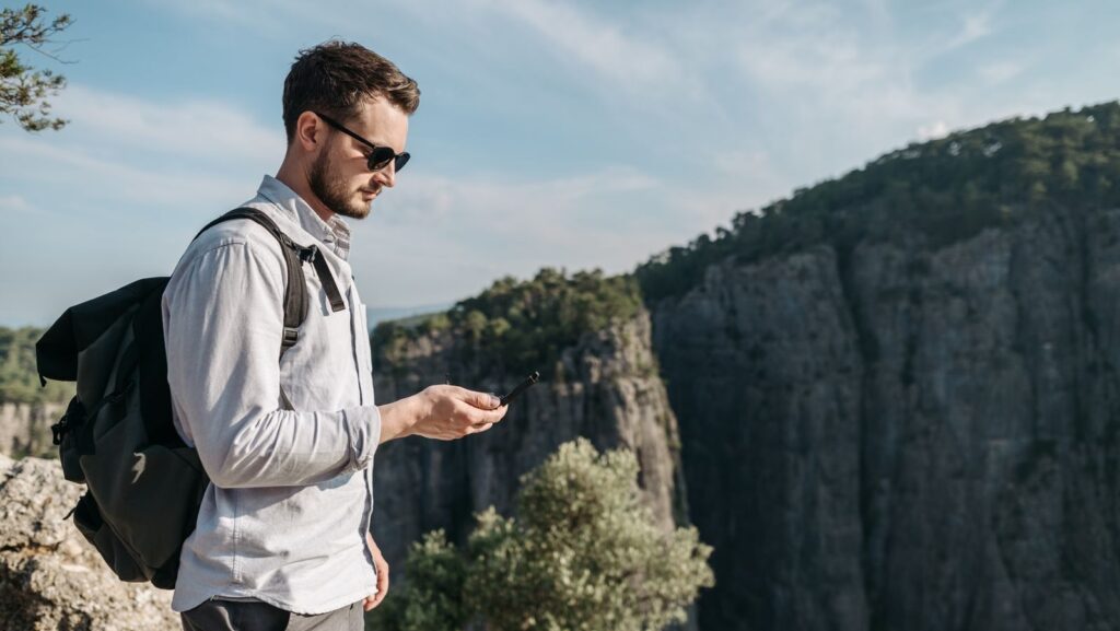 A young man with a backpack enjoys the rugged mountain scenery during a daytime hike.