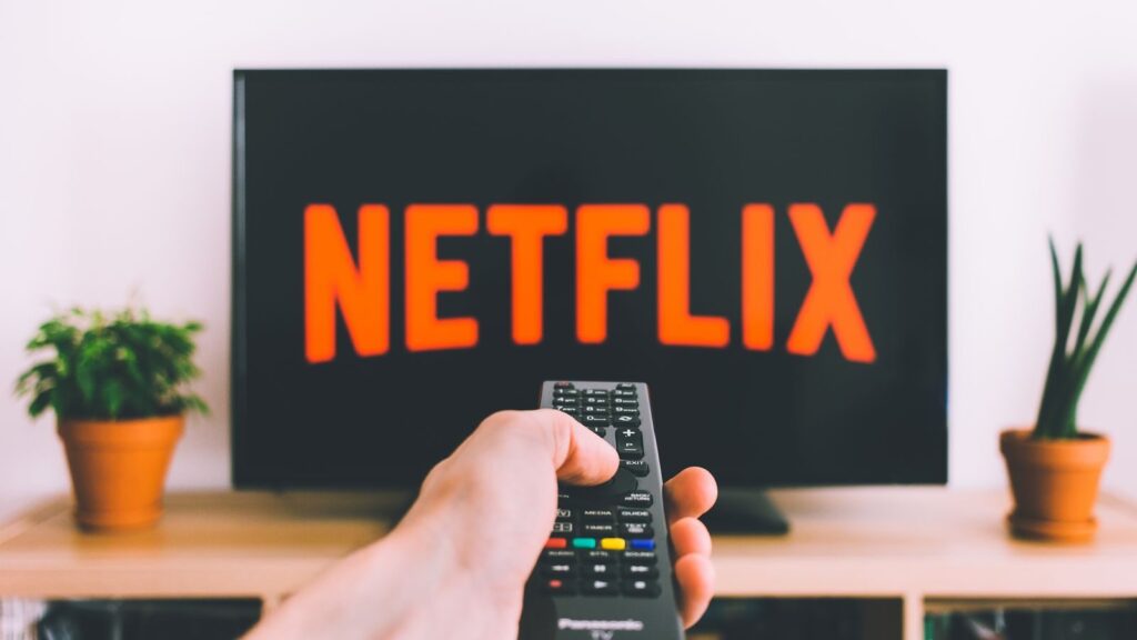 A hand holding a TV remote in front of a screen with Netflix, perfect for streaming and movie night themes.