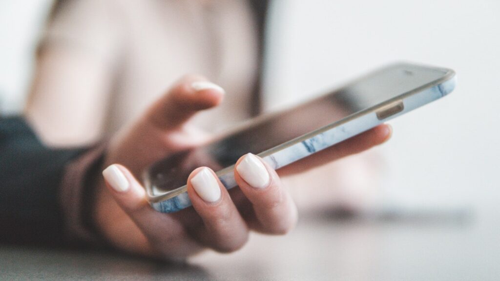 A person holding a smartphone with a marble pattern case in a bright room
