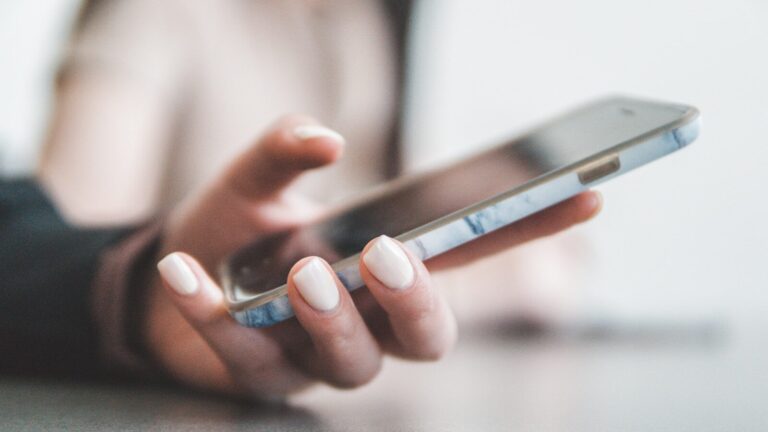 A person holding a smartphone with a marble pattern case in a bright room