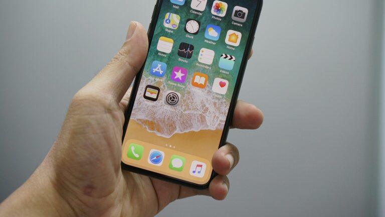 A hand holding a smartphone displaying a home screen with various app icons