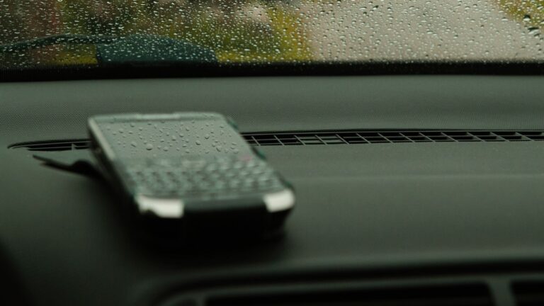 Smartphone on dashboard with raindrop-covered windshield, capturing rainy day essence.