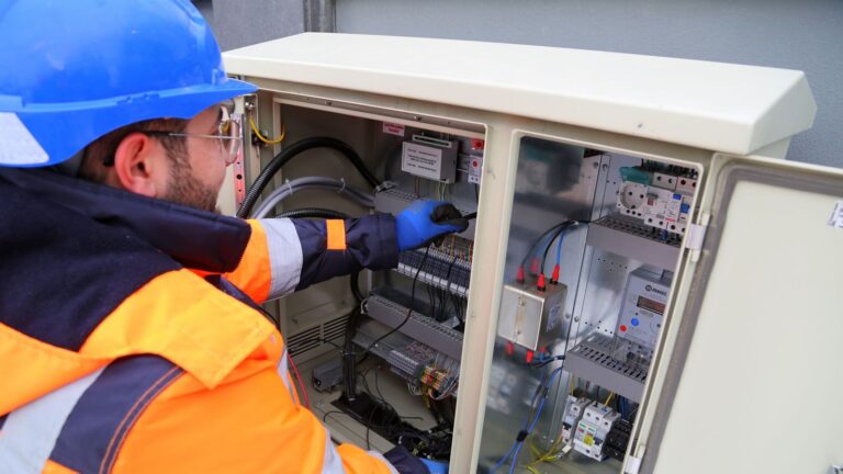 Engineer in safety gear working on an outdoor electrical panel, ensuring system functionality.