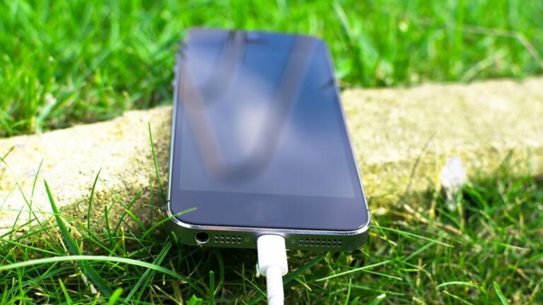 Close-up of a smartphone charging on a grassy lawn, highlighting modern technology in nature.