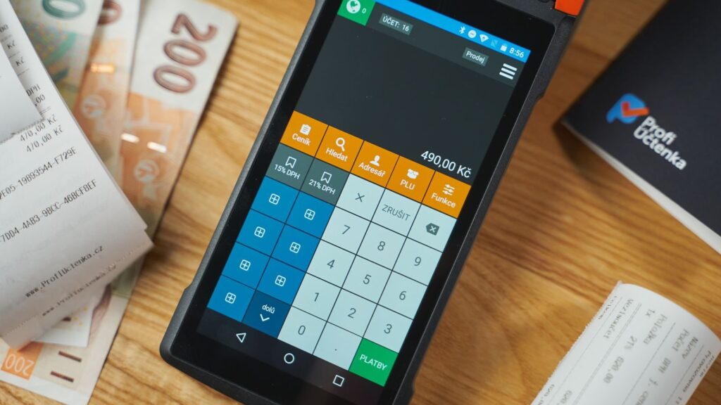 Close-up of a digital payment terminal on a wooden desk with receipts and currency notes.