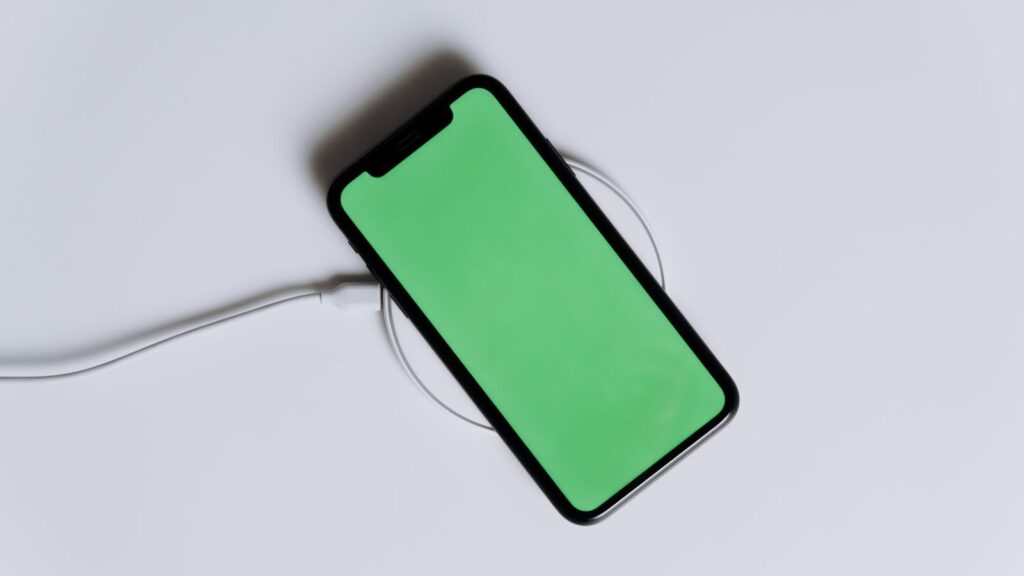 A minimalist smartphone with a green screen on a wireless charger, ideal for tech mockups.