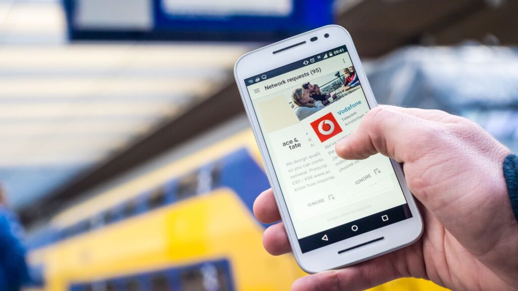 Close-up of a person using a smartphone with a train in the background, outdoors.
