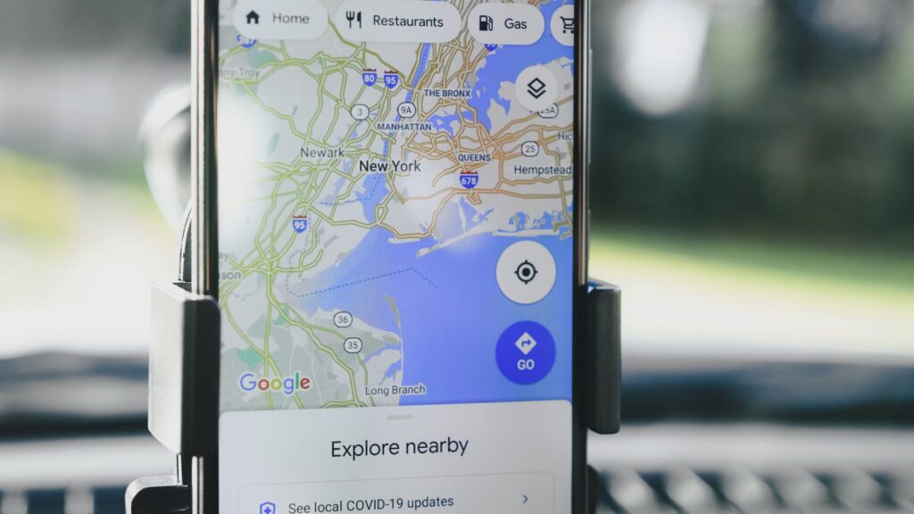 A smartphone displaying GPS map of New York City secured in a car mount during daylight.