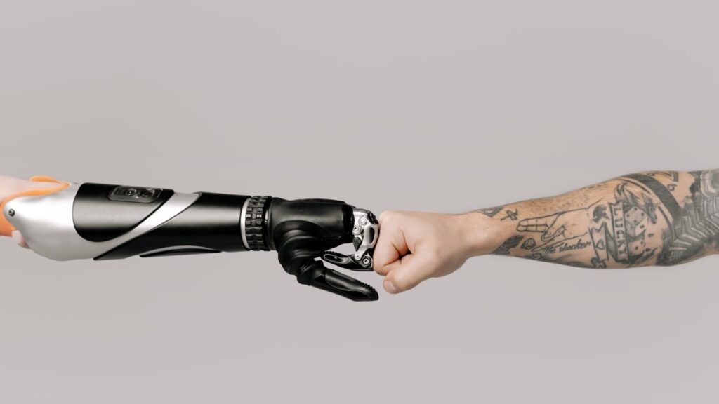Close-up of a tattooed arm fist bumping with a robotic prosthetic arm in studio setting.