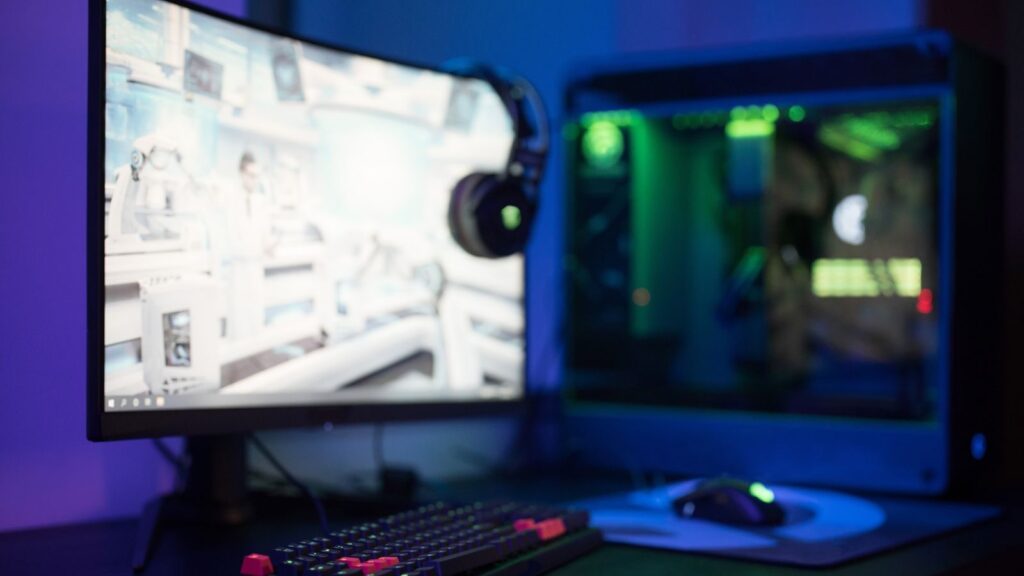 High-tech gaming setup featuring a curved monitor, RGB keyboard, and vibrant lighting.