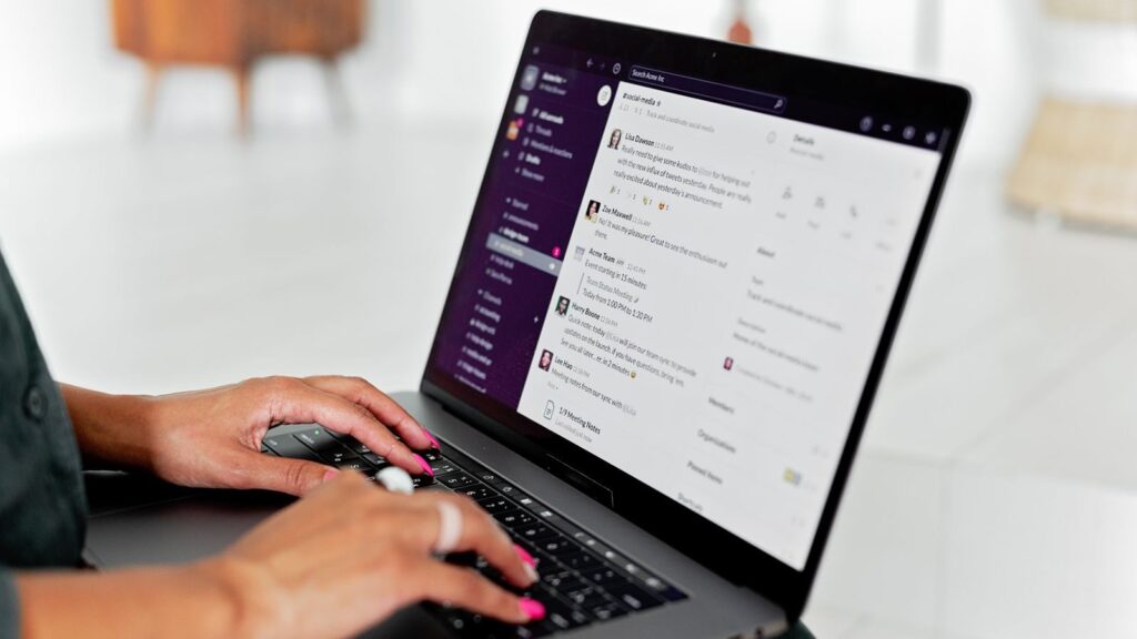 A woman types on a laptop using a messaging app in a modern office setting.