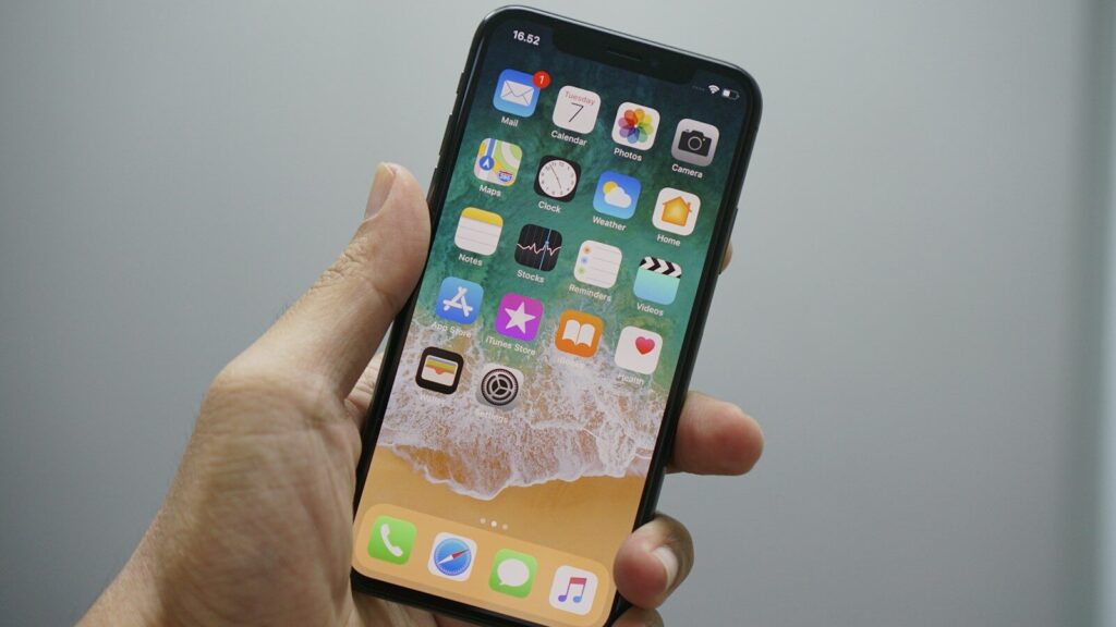 A hand holding a smartphone displaying a home screen with various app icons