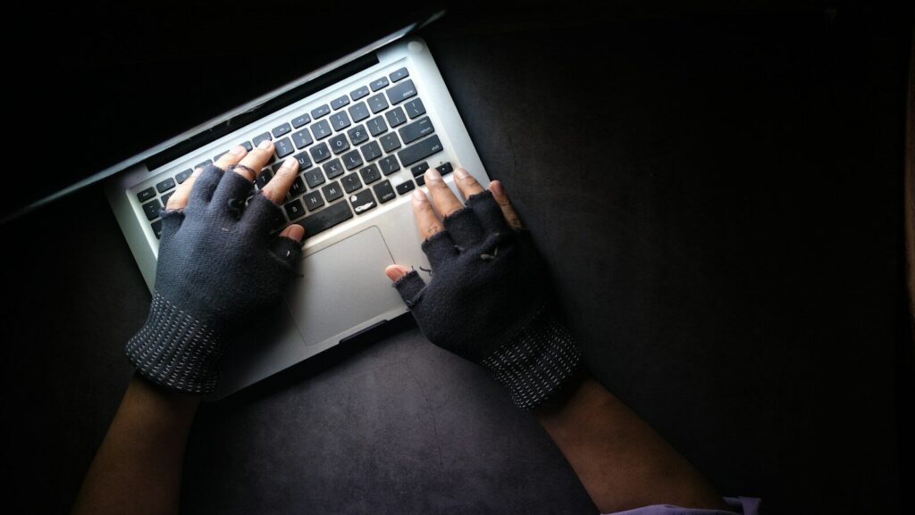 A person wearing fingerless gloves typing on a laptop on a dark surface