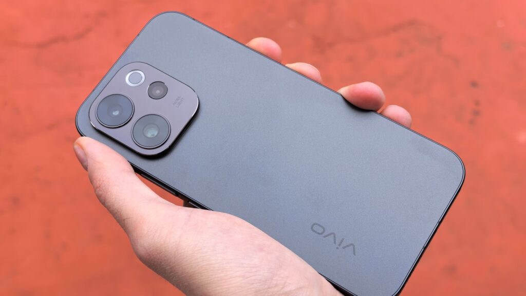 A close-up view of a hand holding a sleek smartphone, captured outdoors against a warm backdrop.