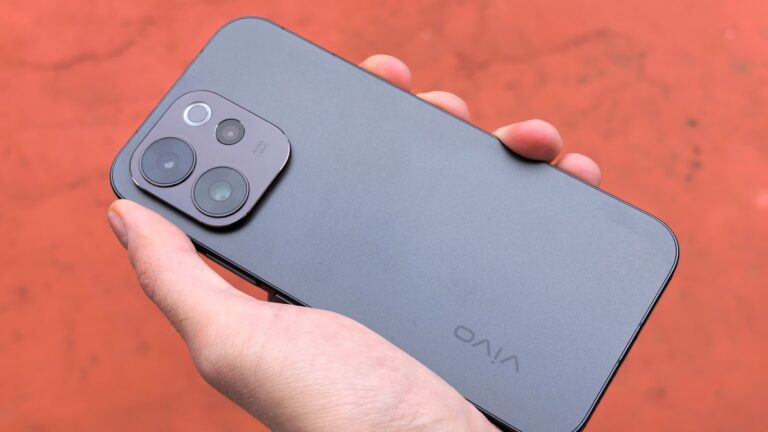 A close-up view of a hand holding a sleek smartphone, captured outdoors against a warm backdrop.