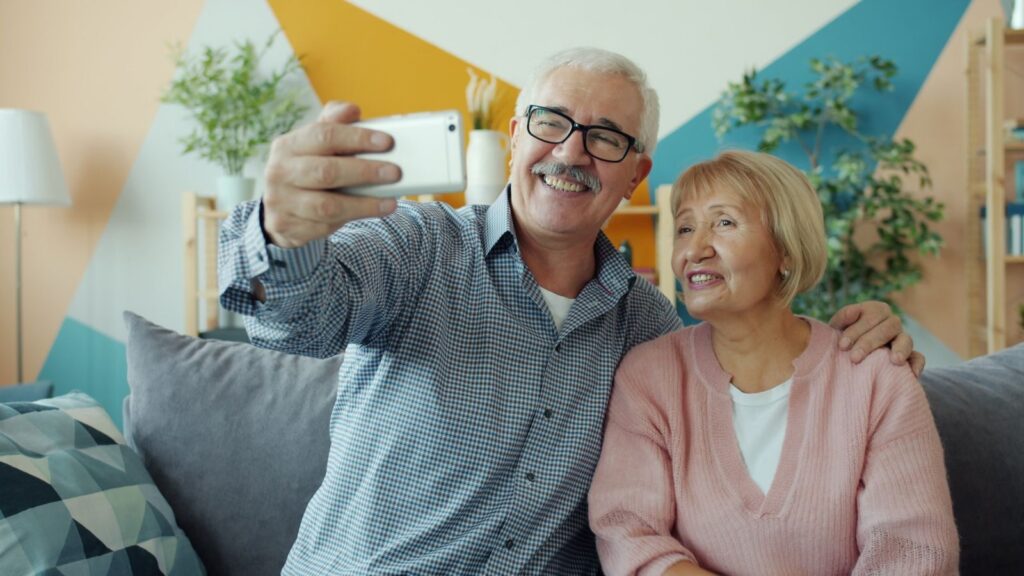 Elderly couple enjoying a selfie together indoors on a cozy couch.