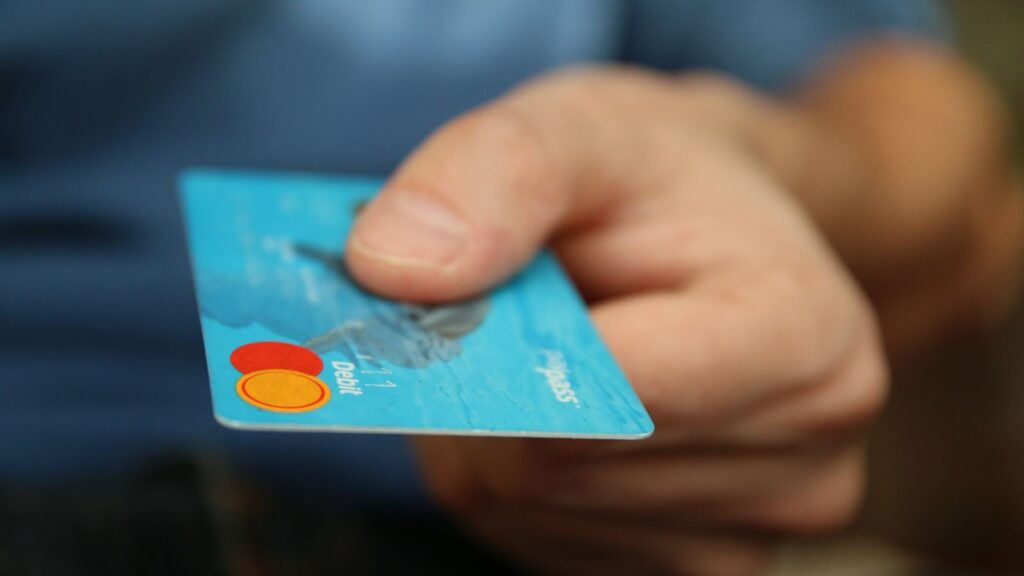 A close-up shot of a hand offering a blue debit card for payment.