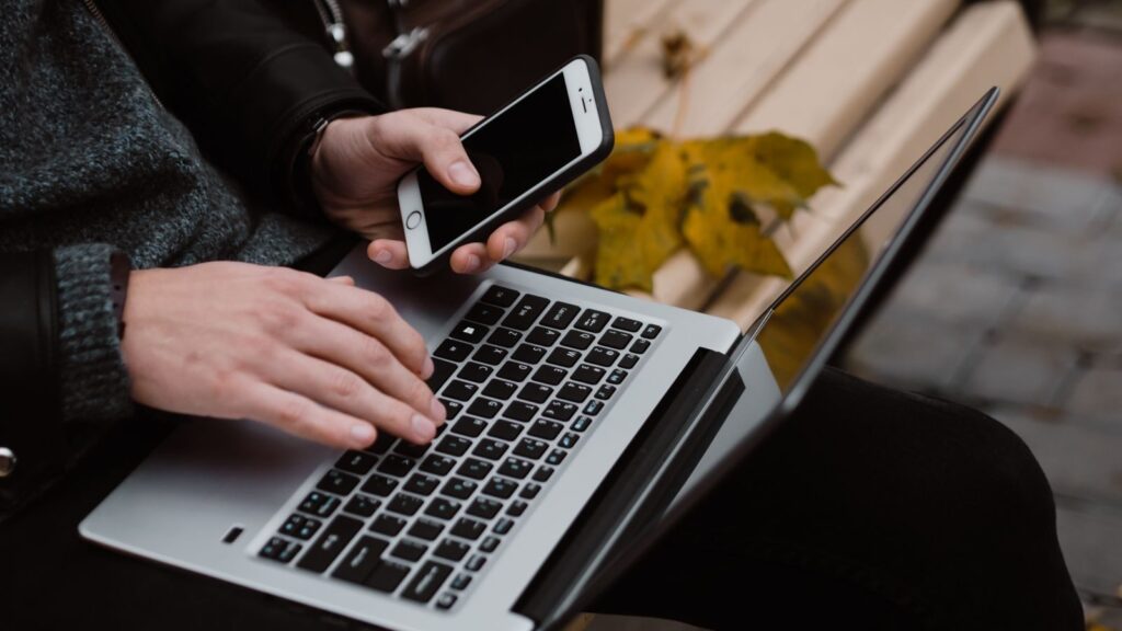 Person working remotely using a laptop and smartphone outdoors, embodying digital nomad lifestyle.