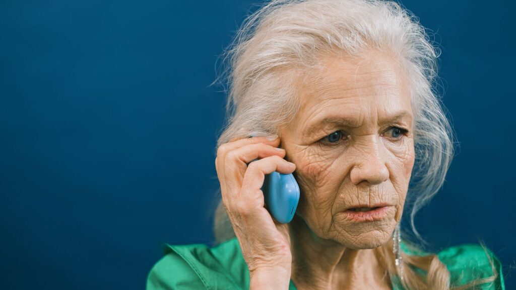Senior woman with gray hair talks on mobile phone against a blue background.